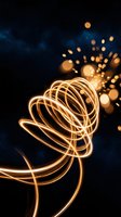 Glowing golden light trails spiral upward with sparkling bokeh particles on a dark cosmic background, evoking energy, motion, and celebration.
