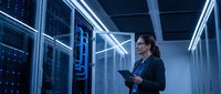 Professional woman IT specialist working with tablet in modern server room with glowing blue LED lights and network equipment for technology solutions.