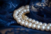 Elegant white pearl necklace with golden clasp on dark blue lace fabric background, creating luxurious contrast for jewelry photography and fashion accessories.