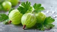 Fresh green gooseberries with water droplets and leaves on rustic wooden surface for healthy eating and organic food concepts.