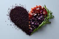 Heart shape made with black quinoa grains, fresh chopped vegetables and herbs including red tomatoes, purple onions and green rosemary on gray background.