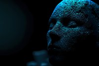 Digital polygonal face emerging from darkness with blue technological illumination, representing artificial intelligence and future technology concepts.