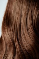 Close-up of smooth, shiny auburn hair with gentle waves showing texture and natural highlights against neutral background.