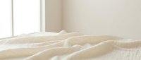 Unmade bed with wrinkled white bedding and soft natural lighting from window creating cozy bedroom atmosphere for interior design concepts.