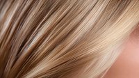 Macro shot of highlighted blonde and brown hair strands showing natural texture and shine, demonstrating professional hair coloring and styling techniques.