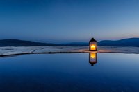 Glowing lantern creates perfect reflection on calm water surface during blue hour twilight with mountain silhouettes in background for peaceful meditation concepts.