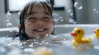 Happy Asian toddler girl enjoying bath time with bubbles and rubber ducks, smiling joyfully in bathtub. Childhood hygiene and playful water activities concept.