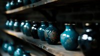Decorative turquoise ceramic vases with golden patterns displayed on wooden shelves in moody lighting, creating atmospheric depth and artistic composition.