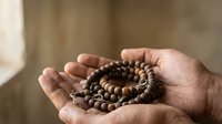 Hands gently holding wooden prayer beads in cupped palms for meditation and spiritual practice in warm natural light.