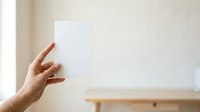 Woman's hand holding blank white card against neutral beige wall background, suitable for mockups, presentations, and advertising campaigns.