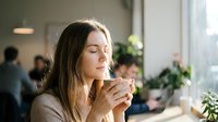 Young blonde woman enjoying hot coffee in modern cafe with peaceful expression and natural lighting for lifestyle and wellness concepts.