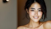 Young Asian woman with natural makeup and glowing skin smiling warmly at camera. Dark hair styled in casual updo against neutral background creates professional portrait.