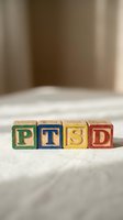 Wooden alphabet blocks spelling PTSD on white fabric surface with neutral beige background, representing post-traumatic stress disorder for mental health awareness.