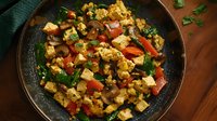 Colorful tofu scramble with mushrooms, bell peppers, and fresh herbs in rustic pan, garnished with parsley. Plant-based breakfast rich in protein and vegetables.