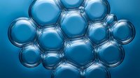 Transparent water bubbles clustered together on a vivid blue background, creating an abstract liquid texture for science or cosmetic design.