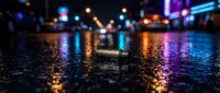 Glowing cylindrical object on wet urban street at night with colorful bokeh lights reflecting on pavement surface for nightlife and city atmosphere designs.