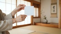 Hands holding blank white card in minimalist interior space with wooden frames and natural light, suitable for business card mockups and promotional designs.