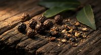 Black peppercorns scattered on rustic wooden surface with green bay leaves, aromatic spices for cooking and seasoning culinary preparations.