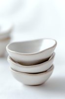Minimalist stacked ceramic bowls in white with organic shapes and subtle texture against bright background, showcasing artisanal craftsmanship and modern design.