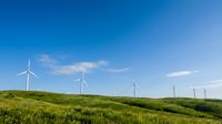 Wind turbines on rolling green hills under clear blue sky, renewable energy landscape for sustainable power generation projects.