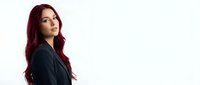 Young professional woman with long burgundy red hair in dark blazer looking over shoulder on white background for business portraits and marketing.