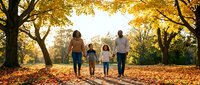 Happy family of four walking hand in hand through autumn park with golden foliage, enjoying quality time together outdoors during fall season.