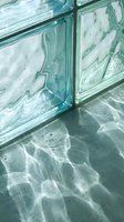 Translucent glass blocks casting rippling water shadows on concrete floor creating abstract light patterns for modern architectural interior design.