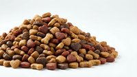 Pile of dry dog food kibble in mixed brown and red colors, isolated on white background for pet nutrition and care concepts.