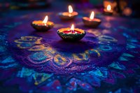 Glowing diya lamps on vibrant blue and purple rangoli pattern during Diwali festival celebration, creating spiritual atmosphere with warm candlelight.