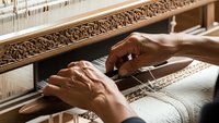 Skilled artisan hands weaving traditional textile on wooden loom, showcasing ancient craftsmanship techniques and cultural heritage preservation methods.