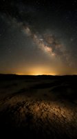 Milky Way galaxy stretching across night sky above desert landscape with golden horizon glow and cracked earth terrain below, suitable for astronomy and nature backgrounds.