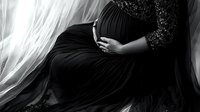 Elegant maternity silhouette in black and white showing pregnant woman in flowing dress gently cradling baby bump against soft window light and delicate lace details.