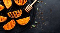 Grilled pumpkin slices with honey drizzle and spices on black cast iron pan. Fresh autumn squash with caramelized grill marks and aromatic herbs.