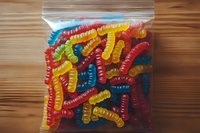 Colorful gummy worms candy in clear plastic bag on wooden surface. Sweet chewy treats for parties, snacks, and confectionery displays.
