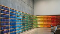 Curved library wall with rainbow gradient of colorful books from blue to red creating vibrant spectrum display in modern reading space.
