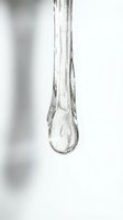 Clear water droplet hanging from glass tube against white background, suitable for science, laboratory, medical, and healthcare applications.