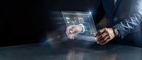 Businessman in dark suit holding transparent digital tablet displaying network connections and data visualization on black background.