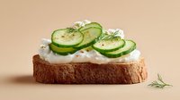 Fresh cucumber slices with cream cheese and dill on artisan bread slice, healthy sandwich appetizer for breakfast or snack on neutral background.