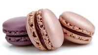 Delicate French macarons in purple and pink pastel colors with creamy filling on white background, showcasing sweet confectionery artistry.