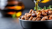 Golden honey drizzling over roasted nuts in dark ceramic bowl, macro food photography with selective focus and warm amber lighting. Fresh herbs garnish.