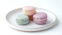 Colorful French macarons in pastel pink, mint green, and lavender arranged on white ceramic plate, sweet meringue sandwich cookies with cream filling.