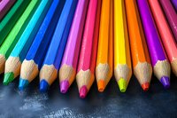 Vibrant colored pencils arranged in rainbow order on dark textured background, sharp tips aligned in row showing wood grain texture and creative art supplies.