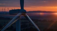 Wind turbine silhouette against a vivid sunset sky, renewable energy concept with rolling hills and wind farm in background.