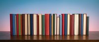 Row of colorful books standing upright on wooden surface against gradient blue to pink background for education and reading concepts.