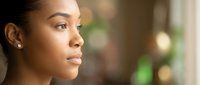 Young African American woman in profile with natural makeup and earrings looking thoughtfully into distance with soft bokeh background lighting.