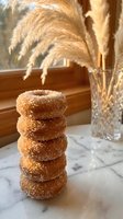 Stack of golden sugar-coated donuts on marble counter with pampas grass decoration in warm sunlight for bakery and cafe marketing.