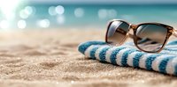 Stylish sunglasses and striped towel on sandy beach with blurred ocean background for summer vacation and travel relaxation concepts.