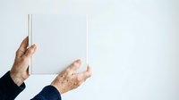 Senior adult hands holding blank white card against neutral background, suitable for greeting cards, business messaging, and promotional campaigns.