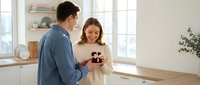 Young couple enjoying morning coffee together in bright modern kitchen with natural light streaming through windows creating warm intimate atmosphere.