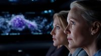 Mature Caucasian woman and younger female colleague in profile view against dark background with glowing data visualization elements, expressing focus and determination.